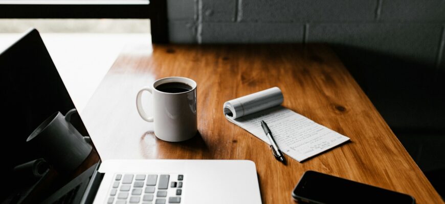 MacBook Pro, white ceramic mug,and black smartphone on table